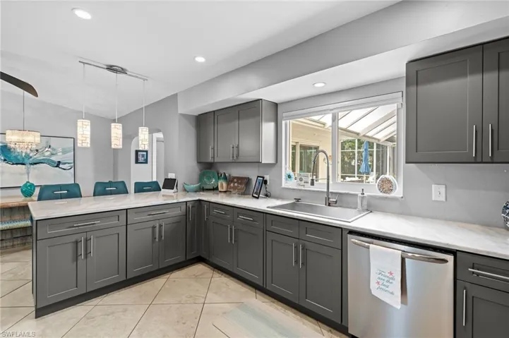 Kitchen featuring hanging light fixtures, gray cabinetry, kitchen peninsula, stainless steel dishwasher, and sink