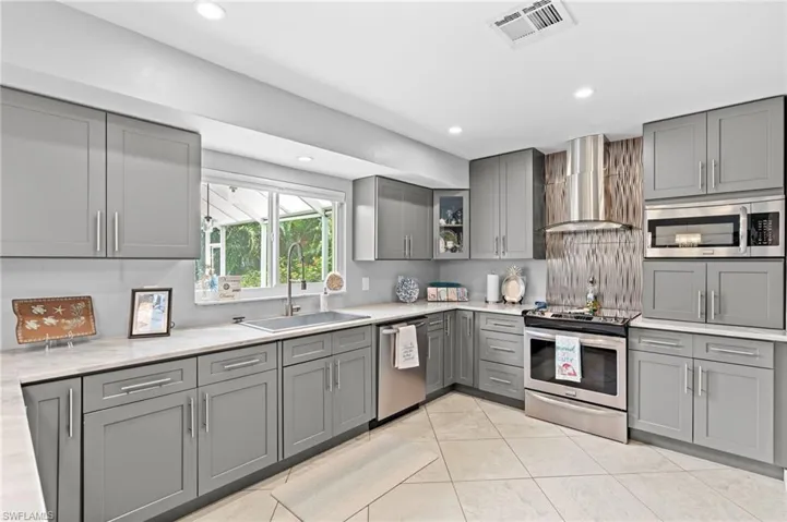 Kitchen with appliances with stainless steel finishes, gray cabinetry, sink, and wall chimney range hood