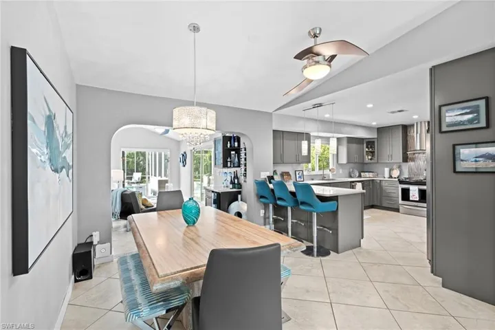 Tiled dining area with a healthy amount of sunlight, ceiling fan with notable chandelier, and vaulted ceiling