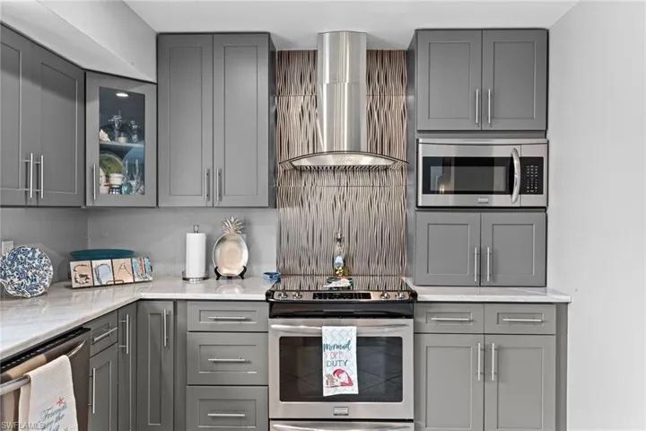Kitchen with light stone countertops, stainless steel appliances, wall chimney range hood, and gray cabinetry