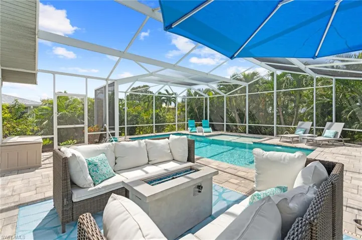 View of pool with a patio, an outdoor living space with a fire pit, and glass enclosure