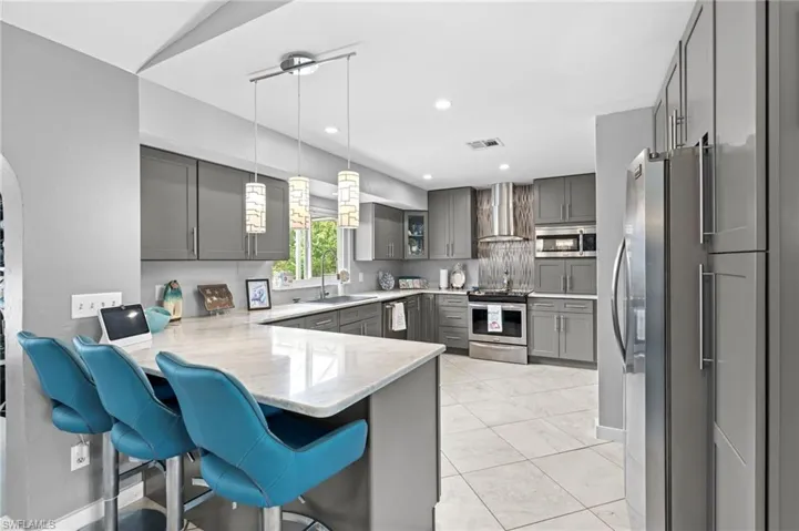 Kitchen with gray cabinets, pendant lighting, kitchen peninsula, wall chimney exhaust hood, and appliances with stainless steel finishes