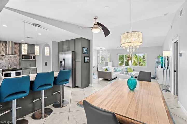 Dining room featuring light tile patterned flooring, ceiling fan with notable chandelier, and vaulted ceiling
