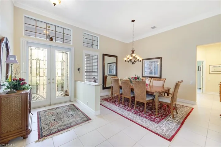 Tiled dining area with ornamental molding, french doors, and a chandelier