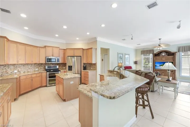 Kitchen with a center island with sink, ornamental molding, sink, appliances with stainless steel finishes, and light stone counters