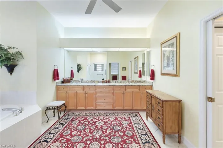 Bathroom with vanity, ceiling fan, tile patterned floors, and tiled bath