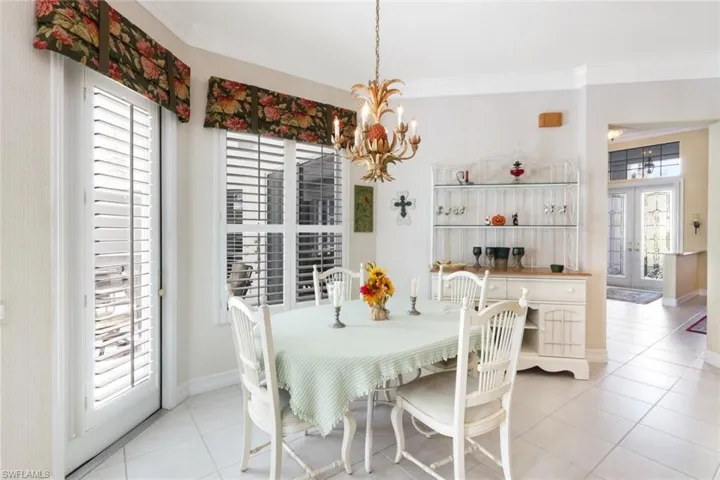 Tiled dining area with french doors, ornamental molding, a wealth of natural light, and an inviting chandelier