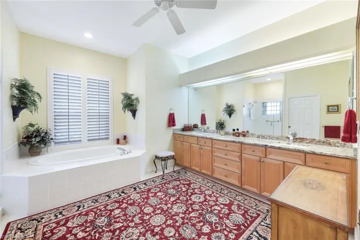 Bathroom with vanity, tile patterned flooring, tiled tub, and ceiling fan