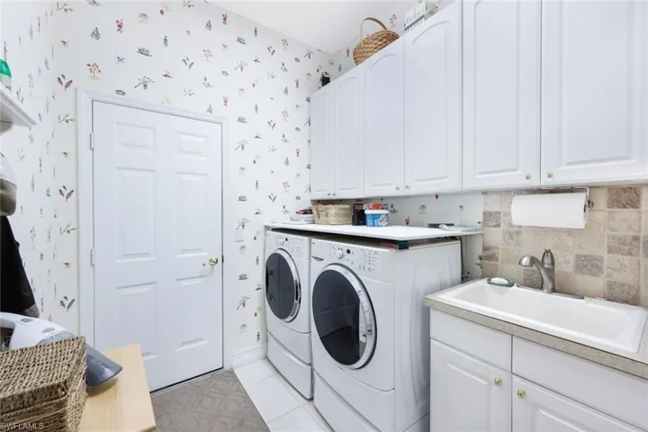 Washroom with cabinets, sink, washing machine and clothes dryer, and light tile patterned floors