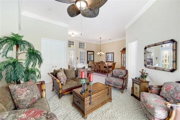 Tiled living room featuring ornamental molding and ceiling fan with notable chandelier
