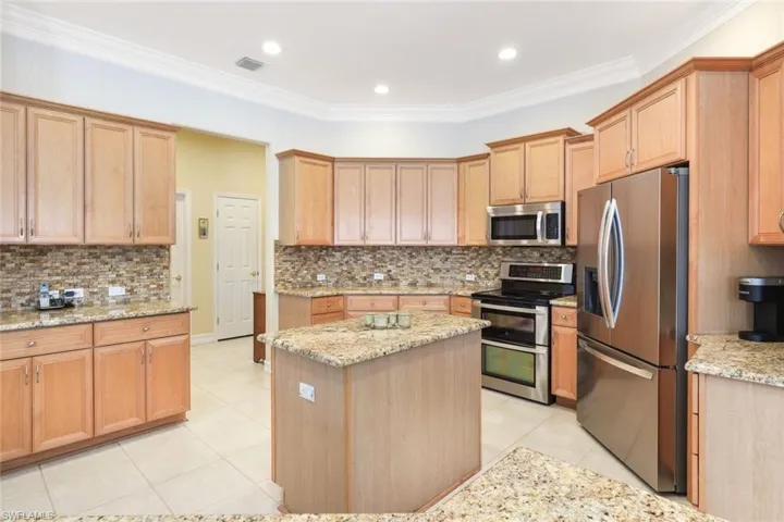 Kitchen featuring crown molding, stainless steel appliances, light stone counters, and backsplash
