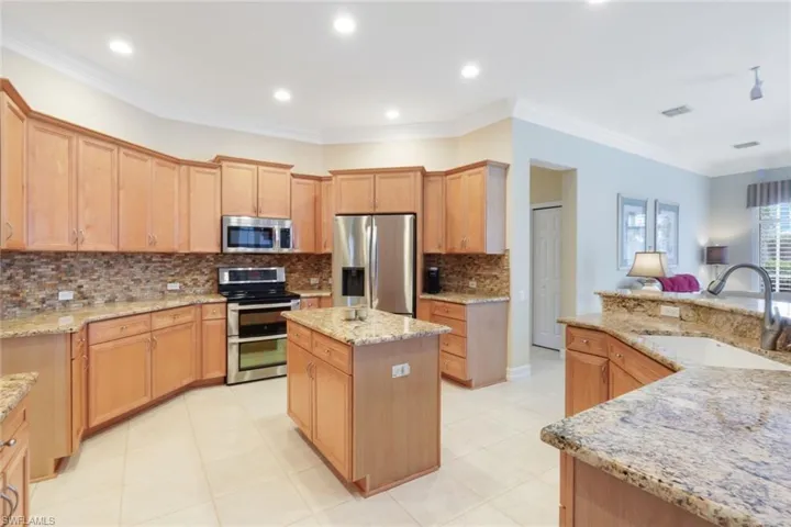 Kitchen featuring light stone countertops, sink, stainless steel appliances, ornamental molding, and a center island with sink