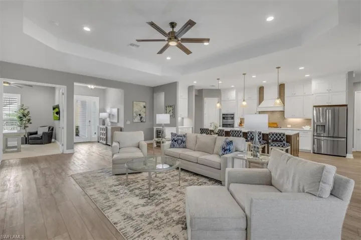 Living room with a raised ceiling, ceiling fan, light ceramic wood finished floors, and recessed lighting