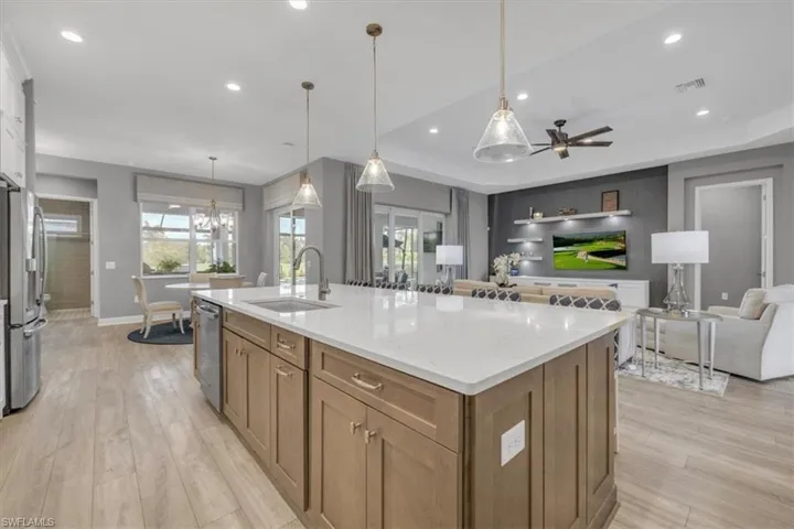 Kitchen featuring brown cabinets, open floor plan, stainless steel appliances, decorative light fixtures, and light stone counters