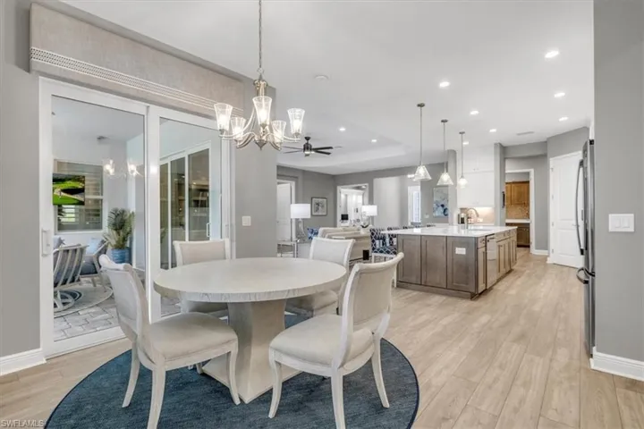 Dining area with light wood-style flooring, a chandelier, recessed lighting, ceiling fan, and a tray ceiling