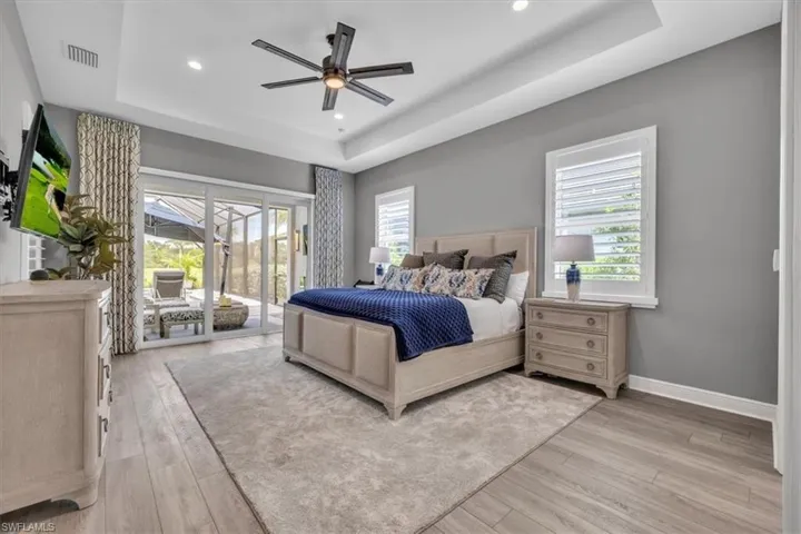 Primary Bedroom featuring a tray ceiling, access to exterior, light wood finished floors, and recessed lighting