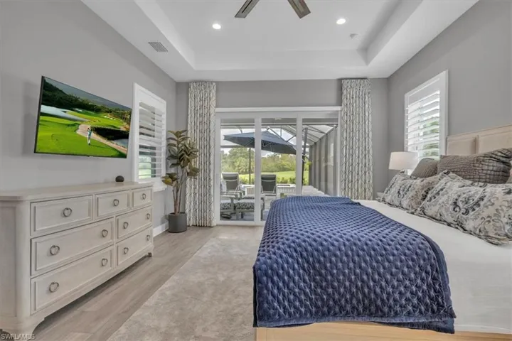Primary Bedroom with access to outside, a raised ceiling, light wood-style floors, a ceiling fan, and recessed lighting