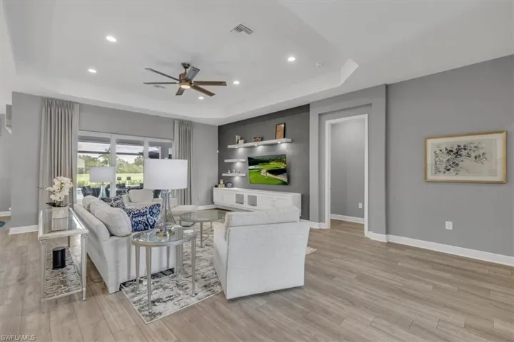 Living area with a tray ceiling, recessed lighting, ceiling fan, and light ceramic wood-style flooring