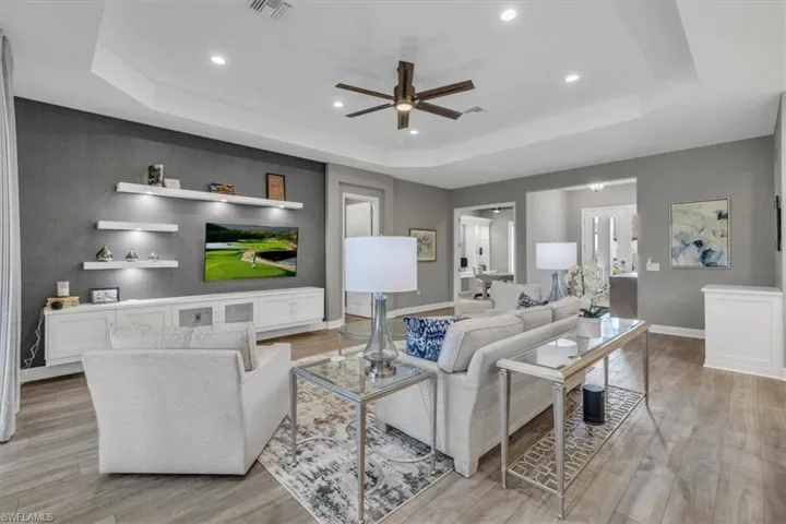 Living area featuring a tray ceiling, a ceiling fan, light wood-type flooring, and recessed lighting