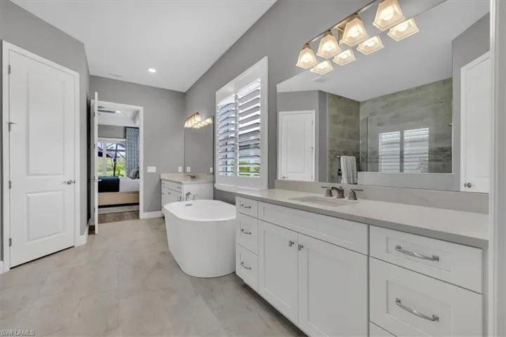 Primary Bathroom featuring two vanities, walk in shower, a freestanding tub, ensuite bath, and light tile patterned flooring