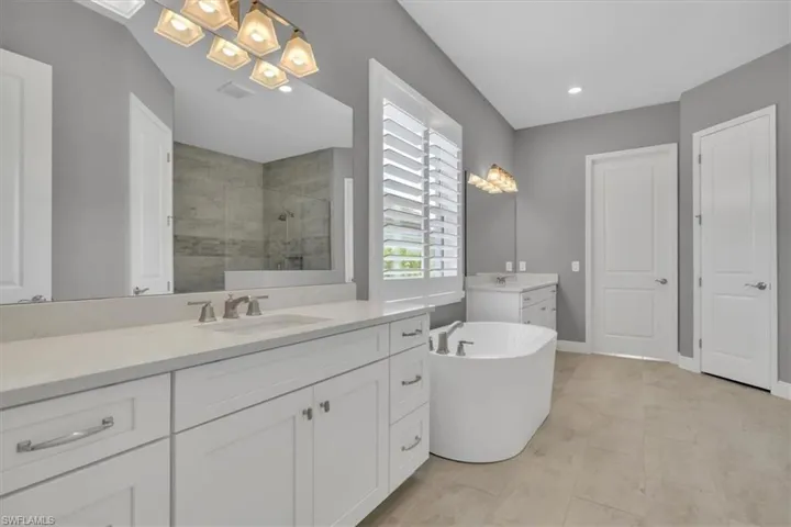 Primary Bathroom featuring two vanities, a stall shower, a freestanding bath, and light tile patterned floors