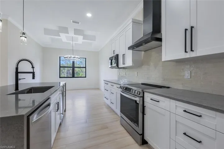 Kitchen with wall chimney range hood, visible vents, dark stone countertops, a sink, and stainless steel appliances