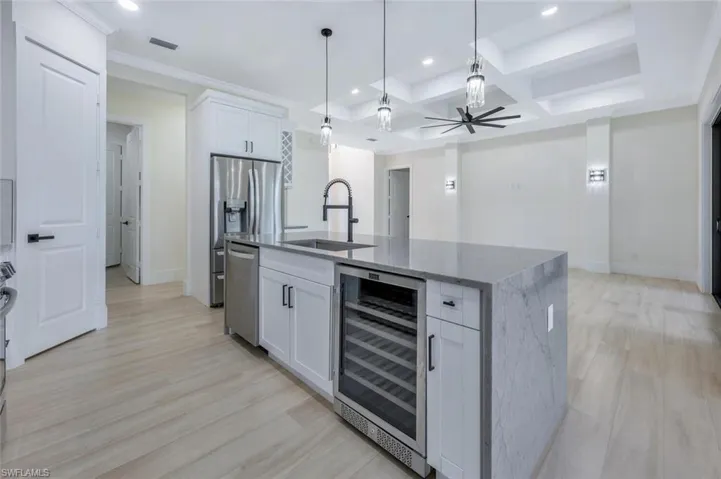 Kitchen featuring visible vents, a kitchen island with sink, a sink, wine cooler, and light wood finished floors