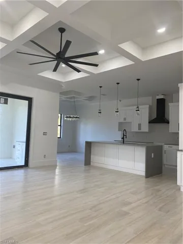 Kitchen with ceiling fan, a kitchen island with sink, coffered ceiling, open floor plan, and range hood