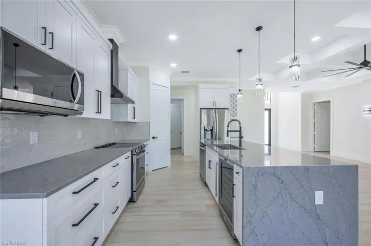 Kitchen featuring wall chimney range hood, a ceiling fan, a sink, stainless steel appliances, and backsplash