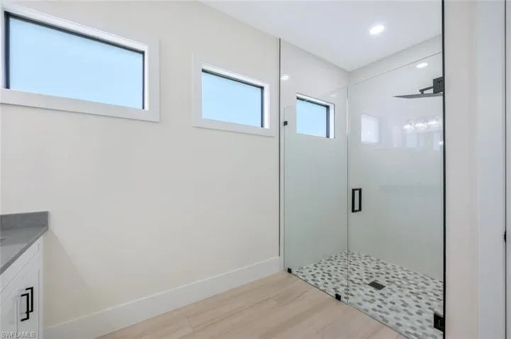 Full bath with a shower stall, vanity, baseboards, and wood finished floors