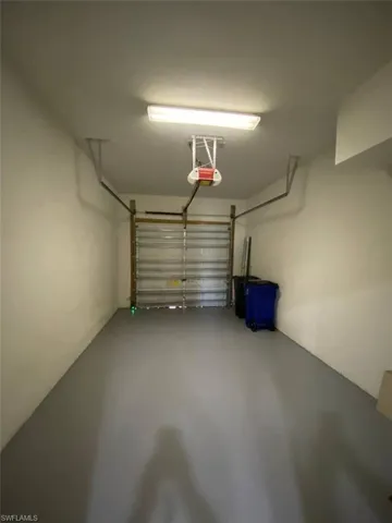 Attached garage with a roll-up door, neutral wall paint, and overhead fluorescent lighting