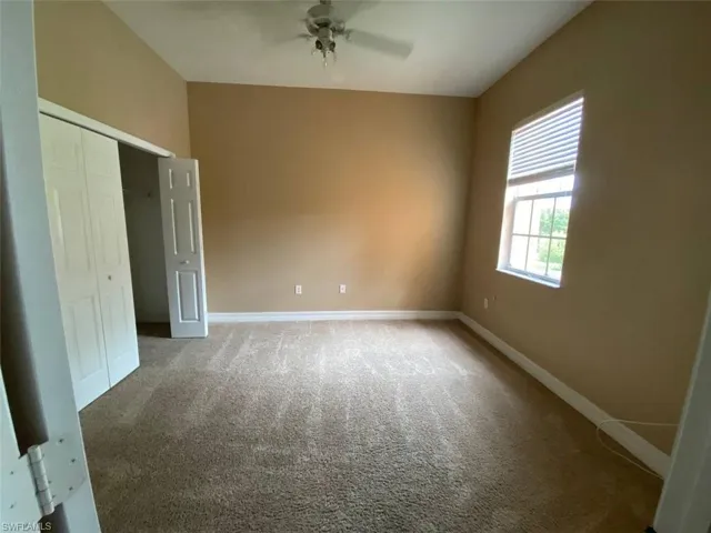 Carpeted room featuring a window with horizontal blinds, bi-fold closet doors, a white ceiling fan, and neutral wall paint