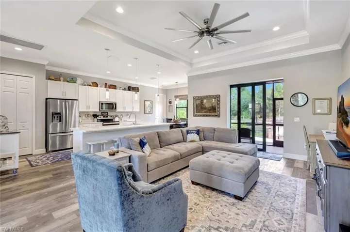 Living area with a tray ceiling, a ceiling fan, recessed lighting, light wood-style floors, and crown molding