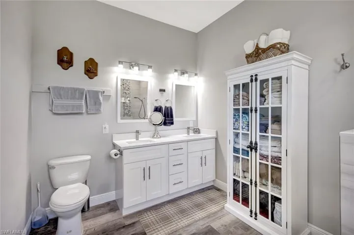 Full bath featuring toilet, wood finished floors, baseboards, double vanity, and a shower