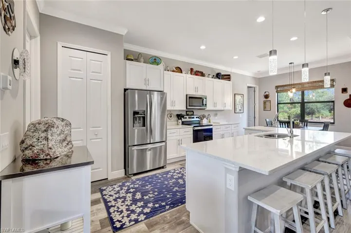 Kitchen featuring appliances with stainless steel finishes, a sink, ornamental molding, white cabinetry, and a breakfast bar