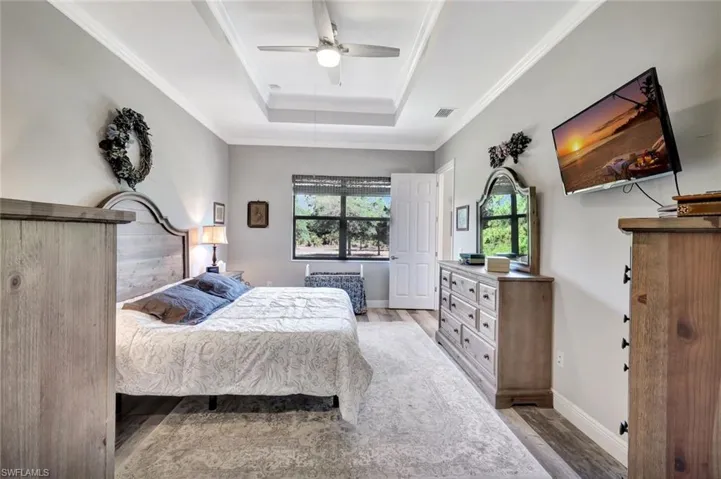 Bedroom featuring wood finished floors, a raised ceiling, crown molding, a ceiling fan, and baseboards
