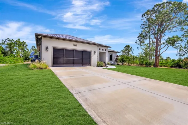 View of front facade with stucco siding, a standing seam roof, driveway, an attached garage, and a front lawn