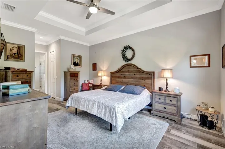 Bedroom featuring a tray ceiling, light wood-style flooring, a closet, baseboards, and crown molding
