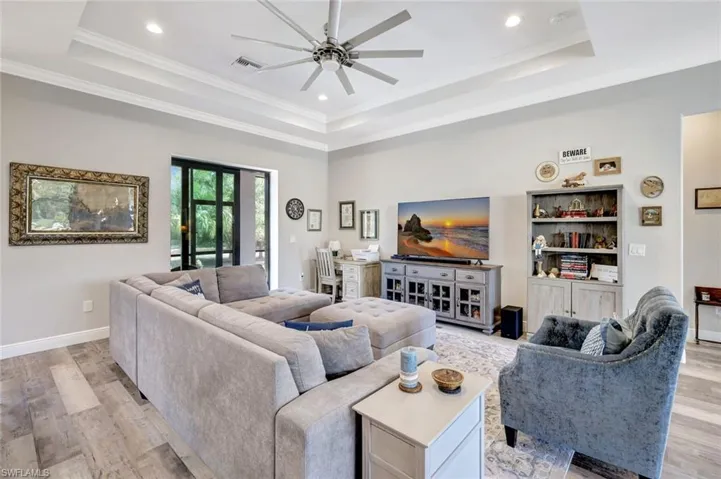 Living room featuring a raised ceiling, light wood-style floors, ceiling fan, recessed lighting, and crown molding