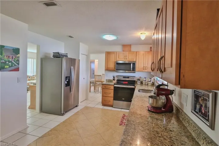 Kitchen with light tile patterned floors, sink, appliances with stainless steel finishes, light stone counters, and a textured ceiling