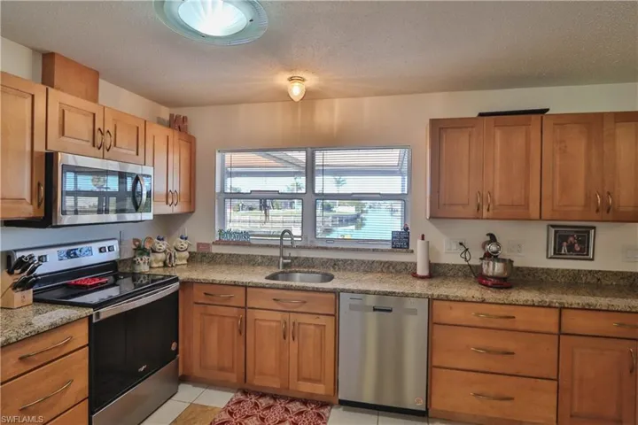 Kitchen featuring sink, light tile patterned floors, a textured ceiling, and appliances with stainless steel finishes
