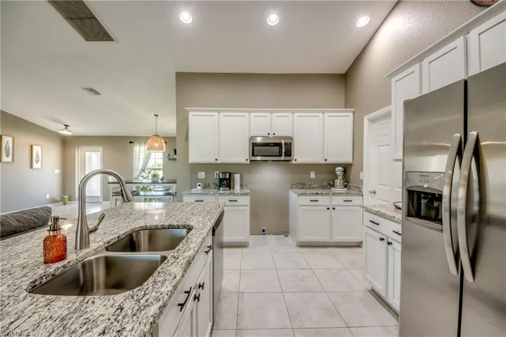 Kitchen with stainless steel appliances, white cabinetry, light stone counters, light tile patterned flooring, and pendant lighting