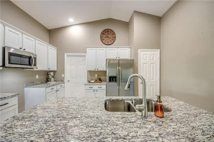 Kitchen with stainless steel appliances, light stone countertops, vaulted ceiling, and white cabinets