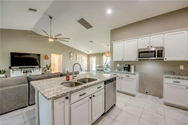 Kitchen featuring stainless steel appliances, a ceiling fan, lofted ceiling, white cabinets, and open floor plan