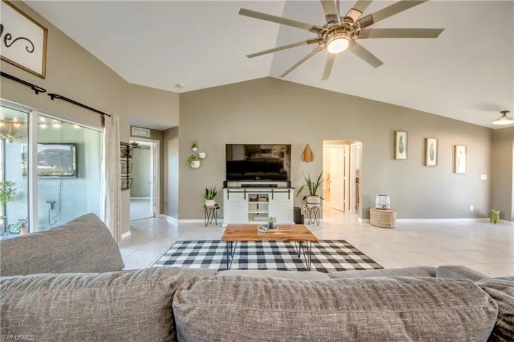 Living room with light tile patterned floors, lofted ceiling, and a ceiling fan