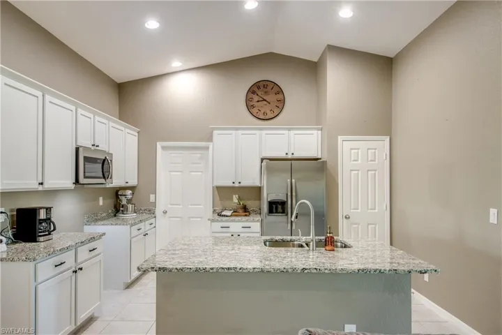 Kitchen featuring stainless steel appliances, light tile patterned flooring, light stone countertops, white cabinets, and a center island with sink