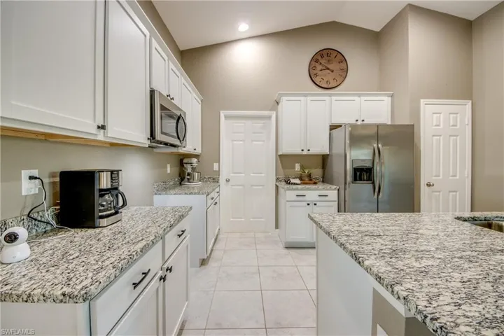 Kitchen with stainless steel appliances, white cabinets, light tile patterned floors, vaulted ceiling, and light stone countertops