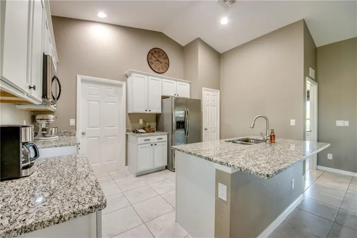Kitchen with appliances with stainless steel finishes, light tile patterned floors, white cabinets, high vaulted ceiling, and a center island with sink