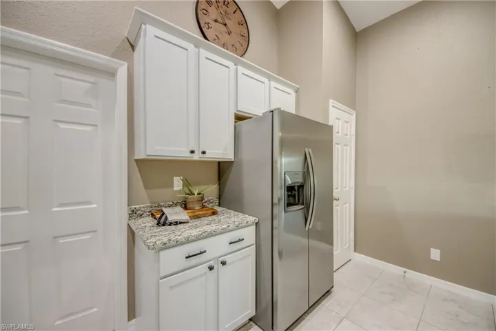 Kitchen with stainless steel fridge with ice dispenser, white cabinetry, light stone countertops, and light tile patterned flooring