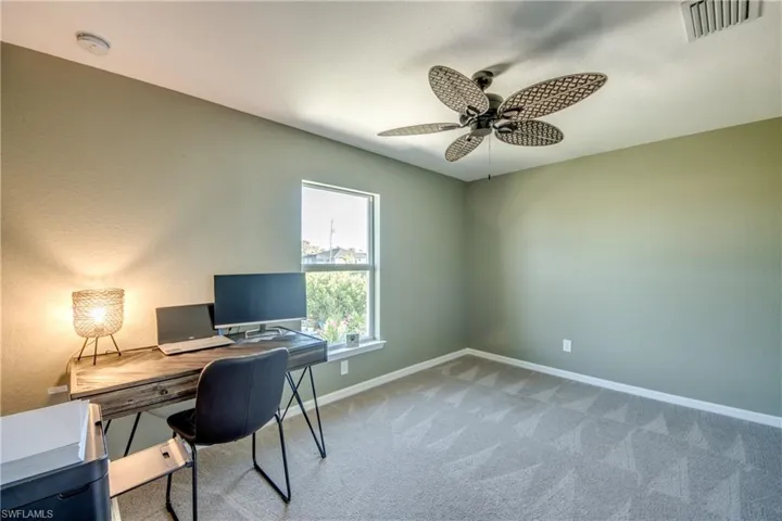 Carpeted home office featuring ceiling fan and baseboards